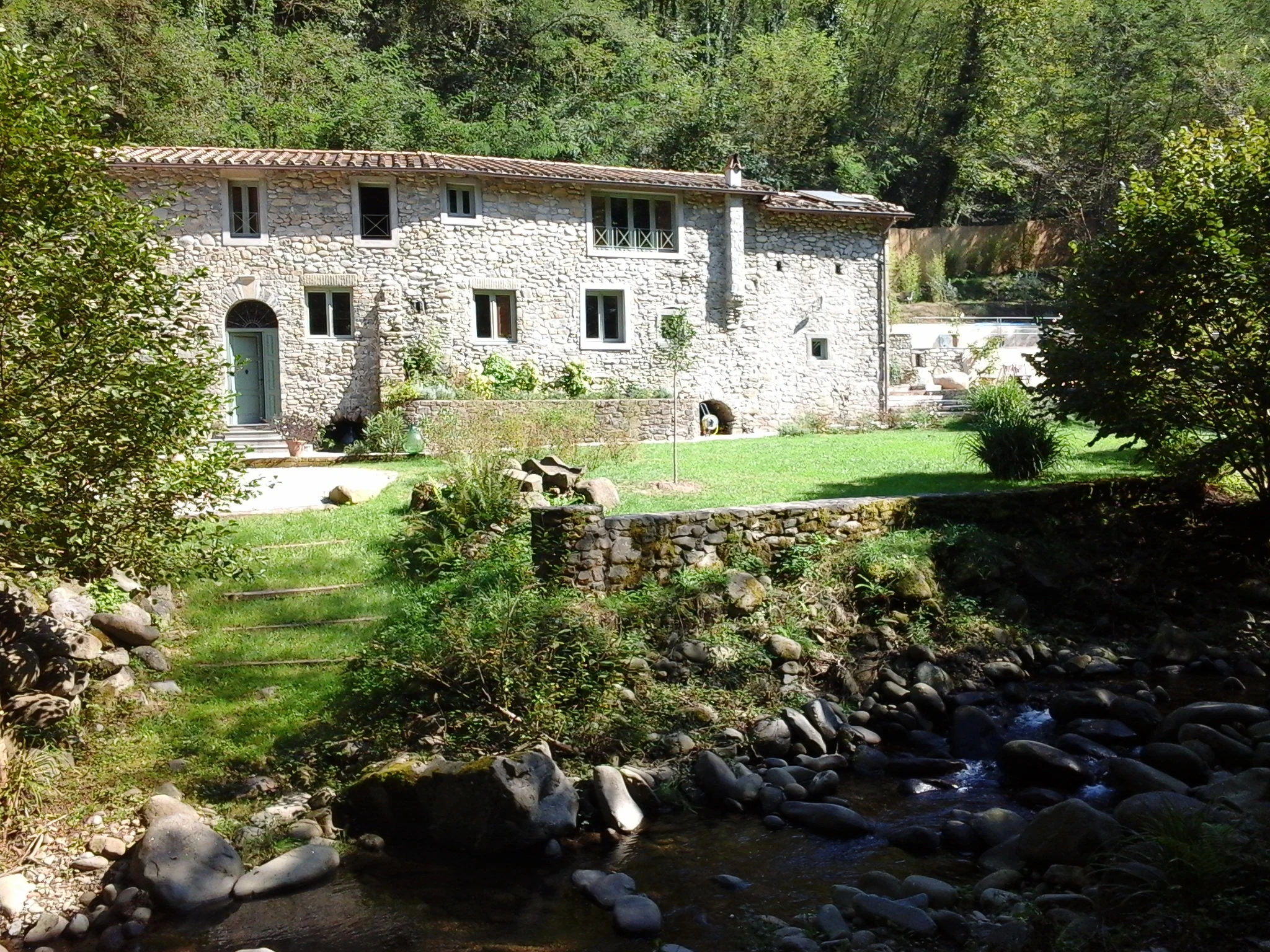 Restored Tuscan millhouse beside a wooded stream and stone bridge