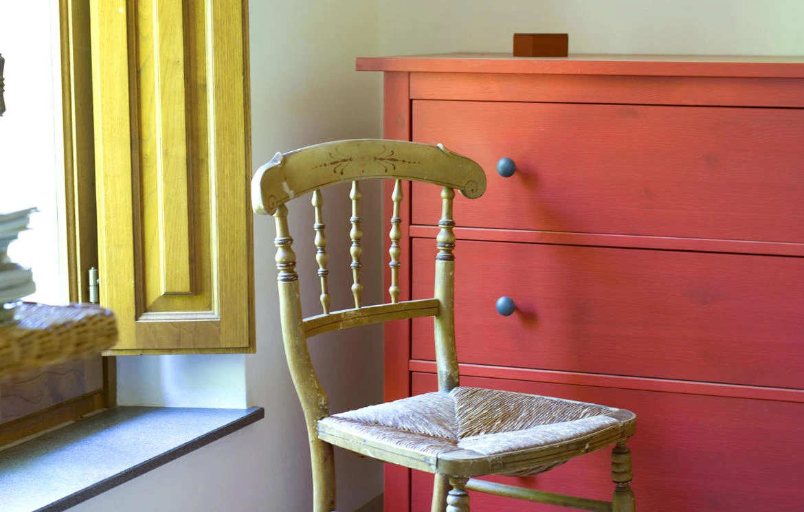 Red chest of drawers and painted chair beside a tall bedroom window