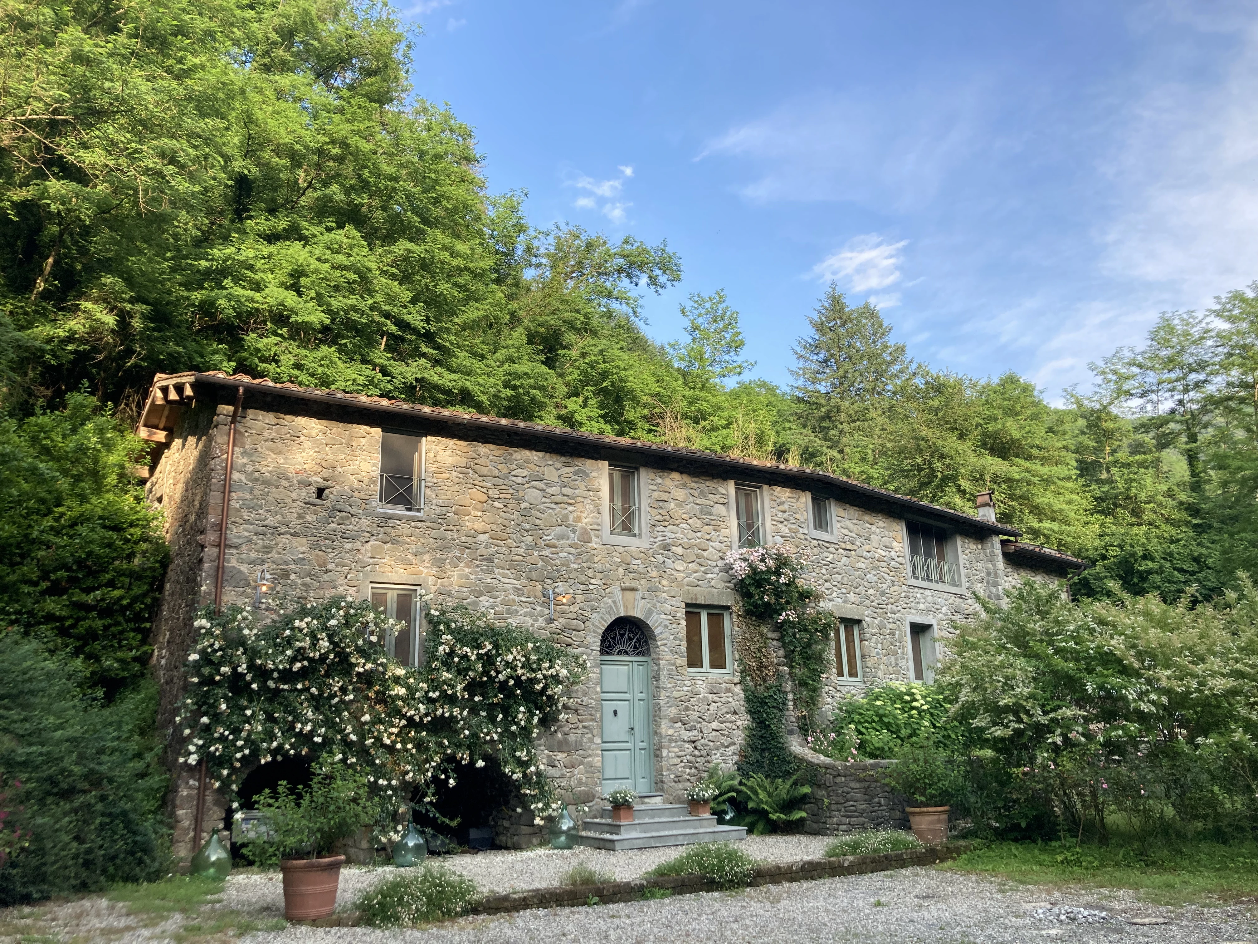 Stone millhouse facade under a blue sky with forest behind