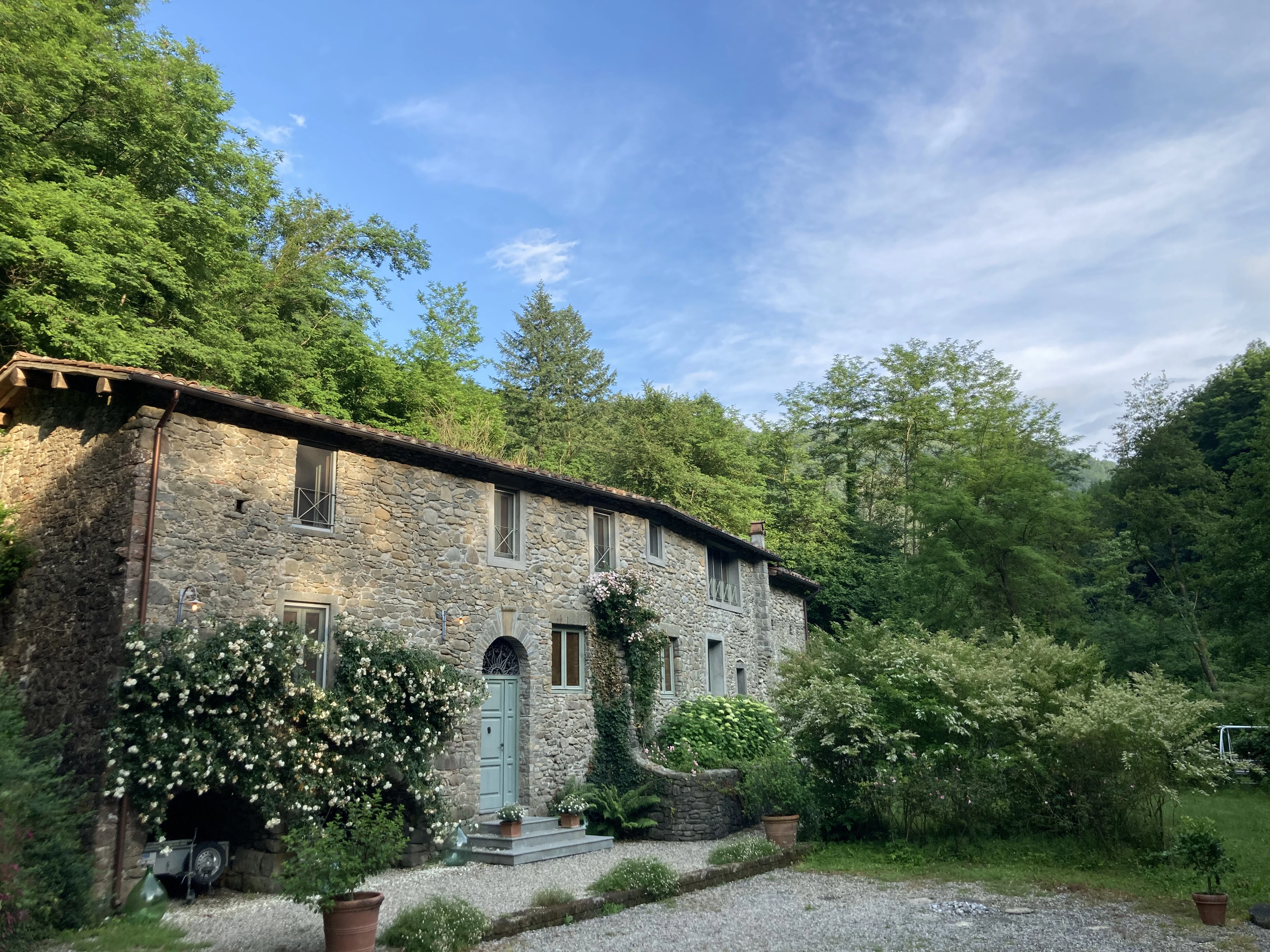 Stone facade of Mulino framed by flowering shrubs and forest