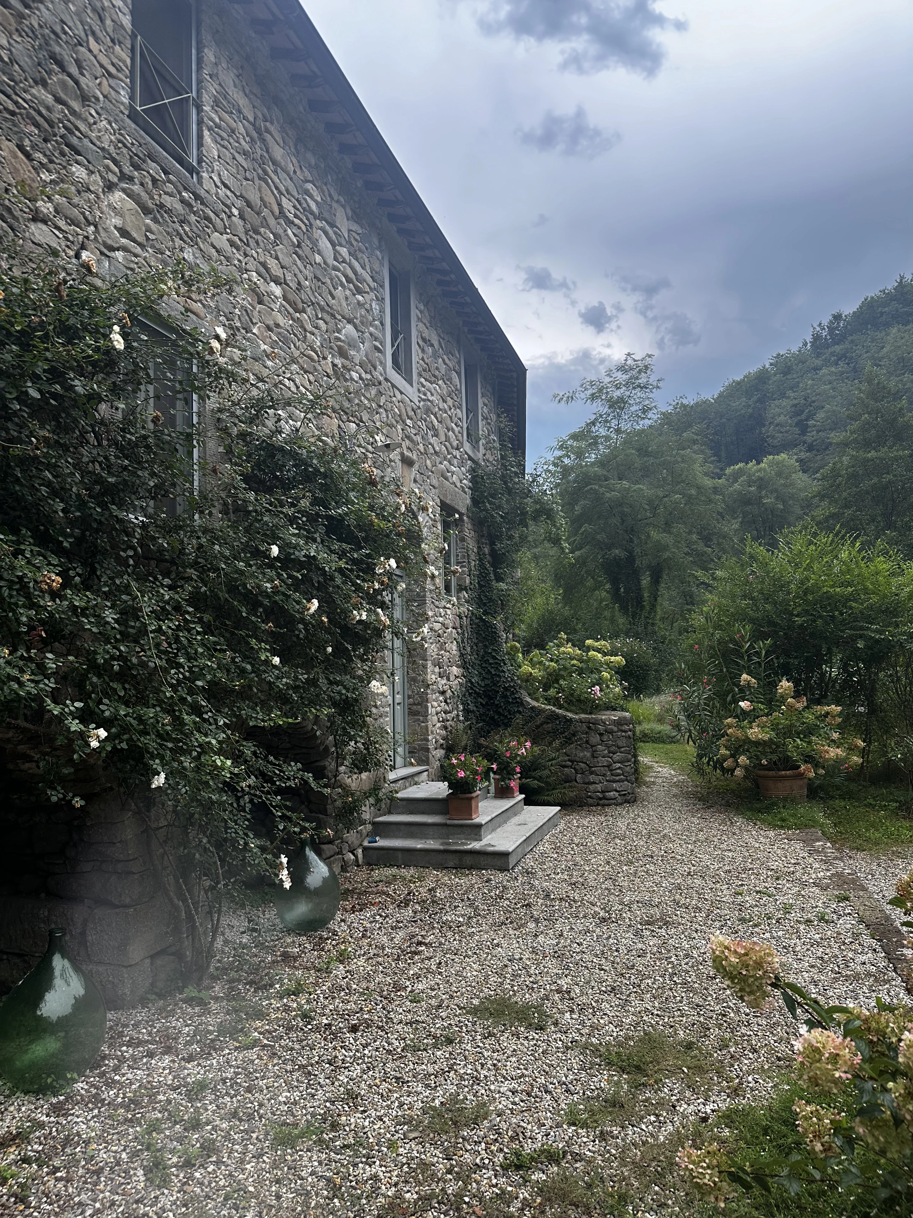 Gravel path beside the stone house with mountain woodland beyond